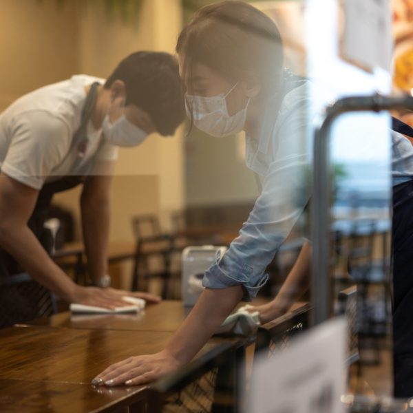Waiter wearing protective face mask while cleaning tables in restaurant
